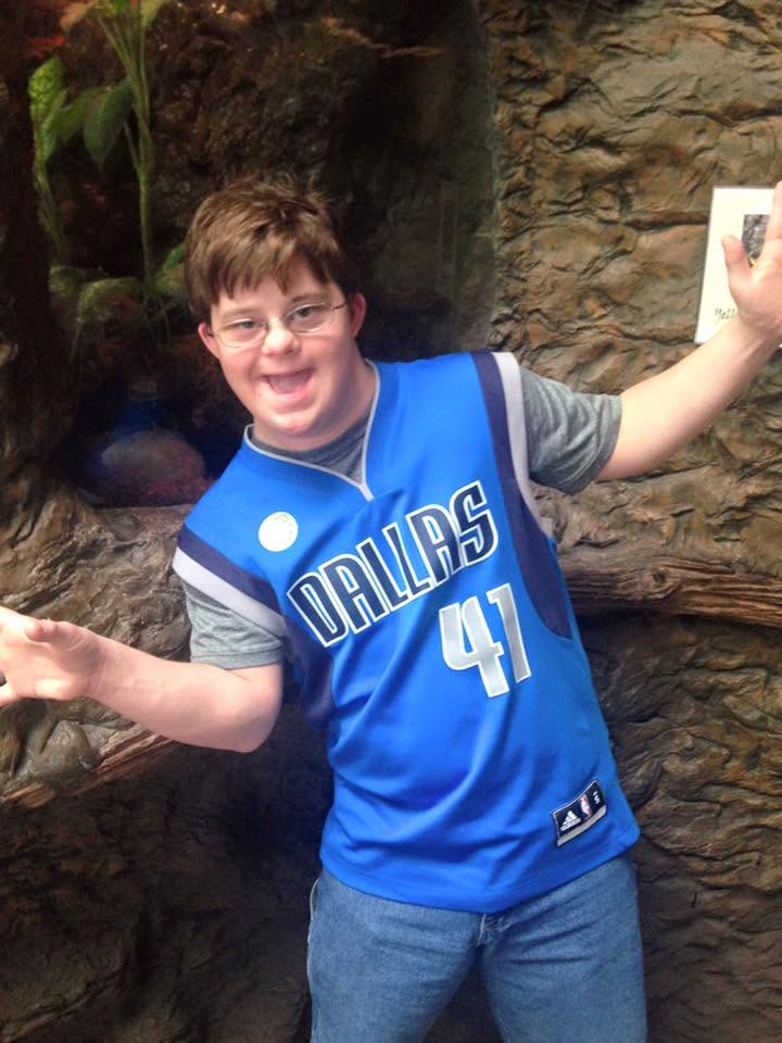 A young man in a Dallas Mavericks jersey smiling with arms outstretched